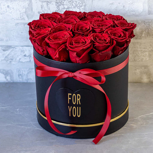 Black box with red roses and a red bow on a gray surface with a light gray background
