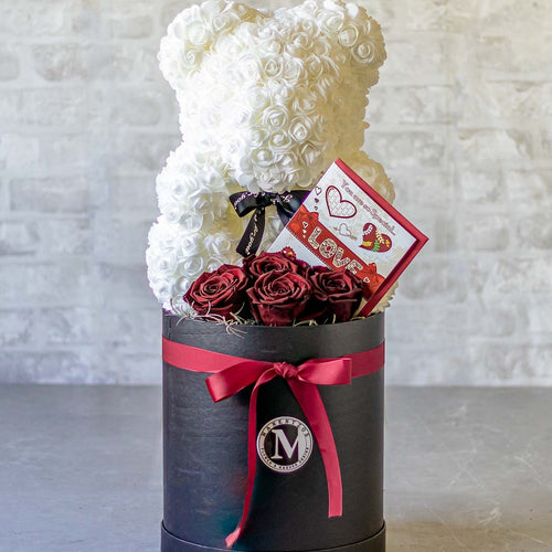 Teddy bear and roses in a black box with a 'Love' card on a light gray background