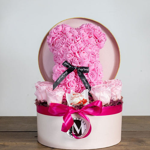 Decorative box with pink roses shaped like a heart and a cake on a wooden surface.
