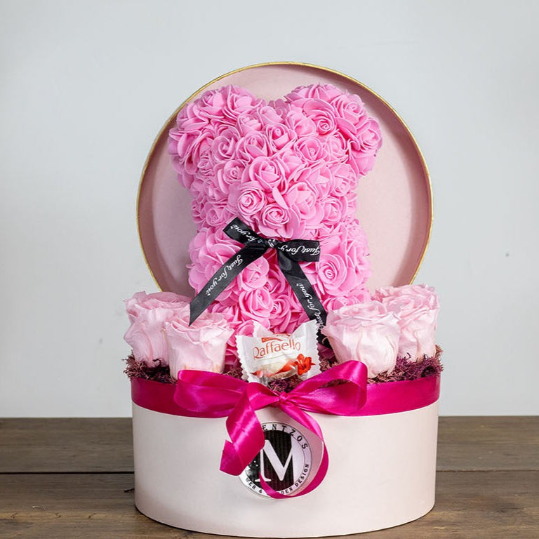 Decorative box with pink roses shaped like a heart and a cake on a wooden surface.