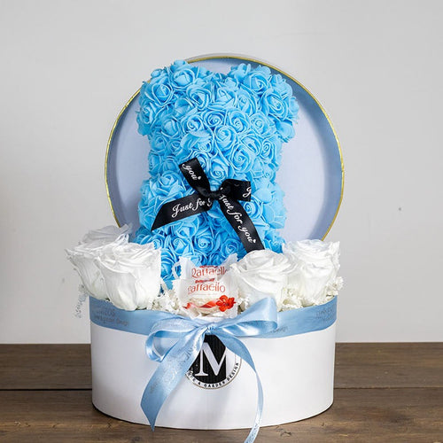Gift box with blue and white flowers and a black bow on a wooden surface.