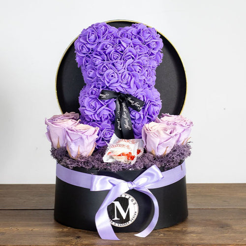 Purple rose teddy bear in a black box with pink roses on a wooden surface