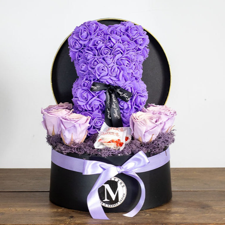 Purple rose teddy bear in a black box with pink roses on a wooden surface