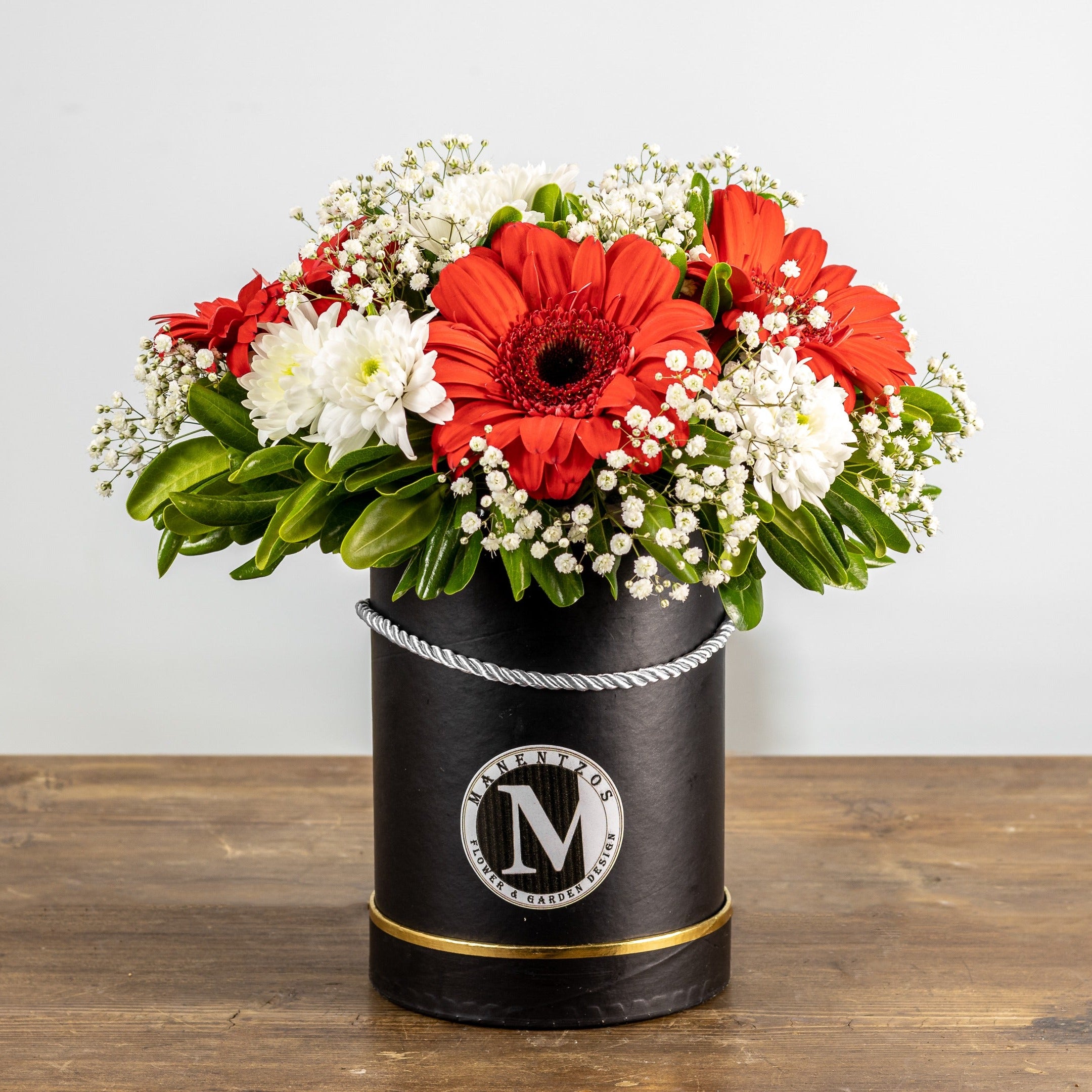 Floral arrangement in a black container with a white logo on a wooden surface and light gray background