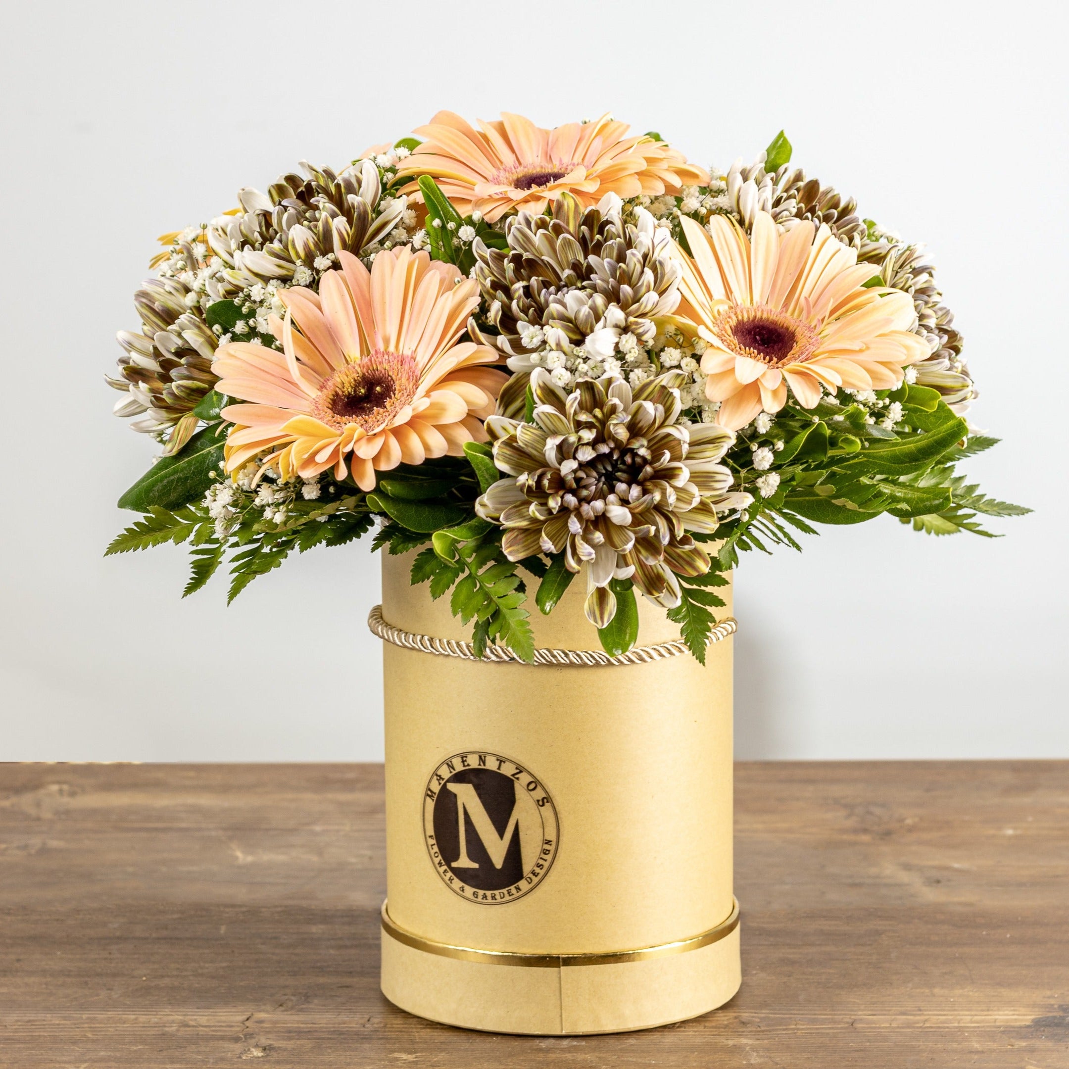 Bouquet of flowers in a gold container on a wooden surface with a white background