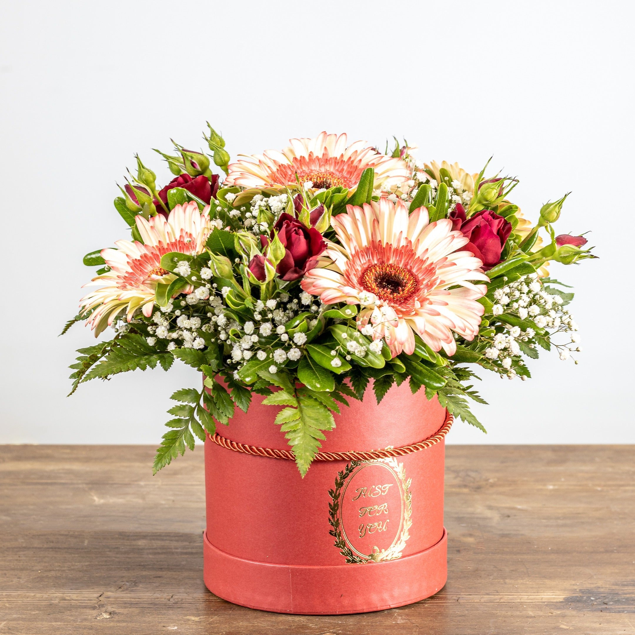 Floral arrangement in a pink box on a wooden surface with a white background