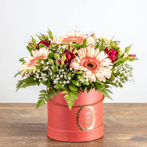 Floral arrangement in a pink box on a wooden surface with a white background
