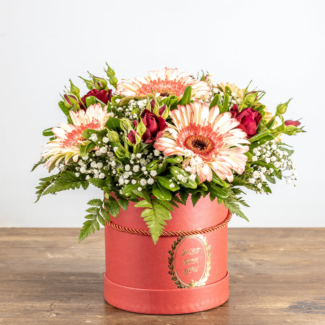 Floral arrangement in a pink box on a wooden surface with a white background