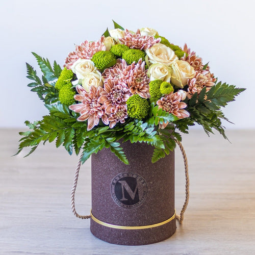 Floral arrangement in a cylindrical container with a visible brand logo on a light background