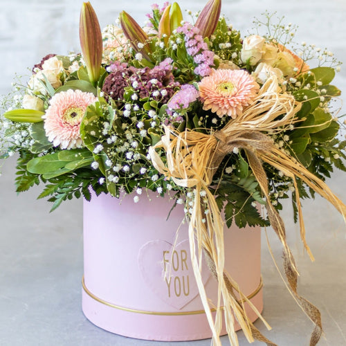 Floral arrangement in a pink box with a gold ribbon on a light background