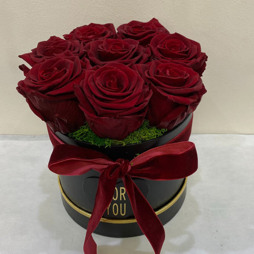 Red roses in a black box with a red bow on a white surface.