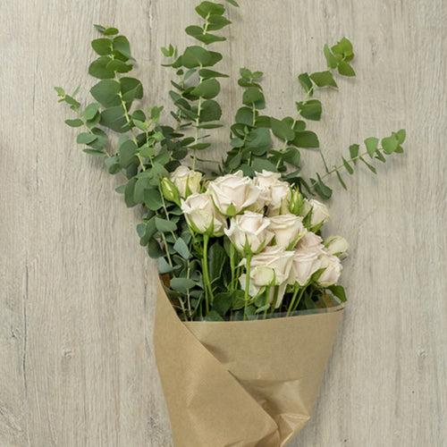 Bouquet of white flowers wrapped in brown paper on a light wooden surface