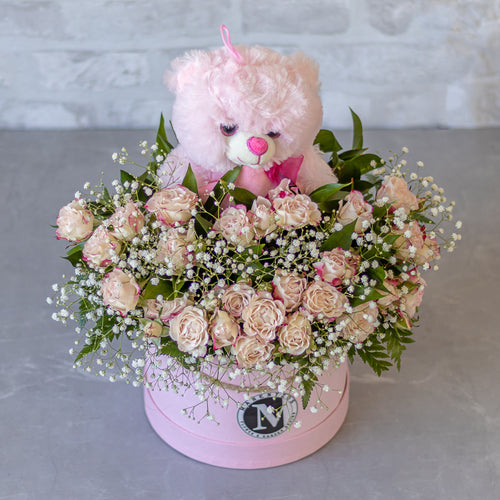 Pink teddy bear with flowers in a box on a gray surface
