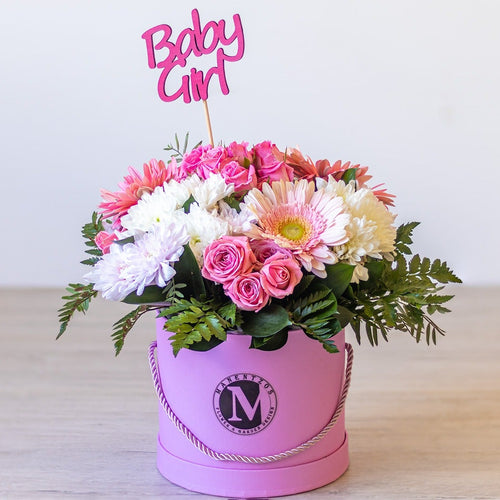 Pink floral arrangement in a box with 'Baby Girl' topper on a light background