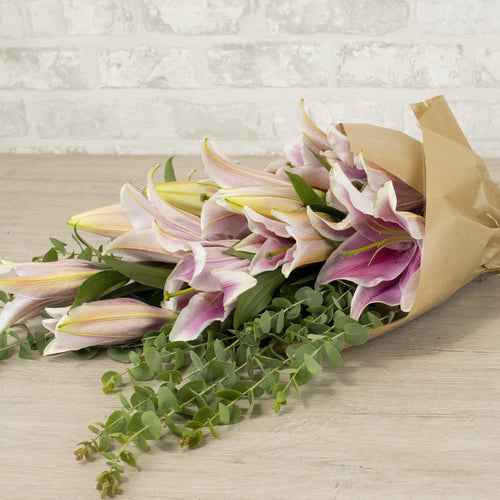 Bouquet of flowers wrapped in brown paper on a wooden surface with a light brick wall background