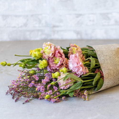 Bouquet of flowers wrapped in brown paper on a light surface with a white background