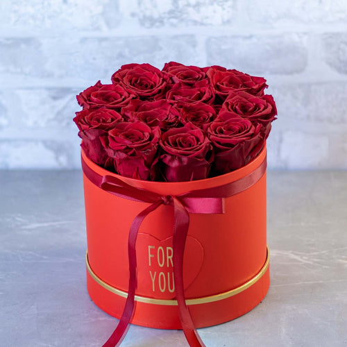Red roses in a round red box with a 'For You' ribbon on a light gray background