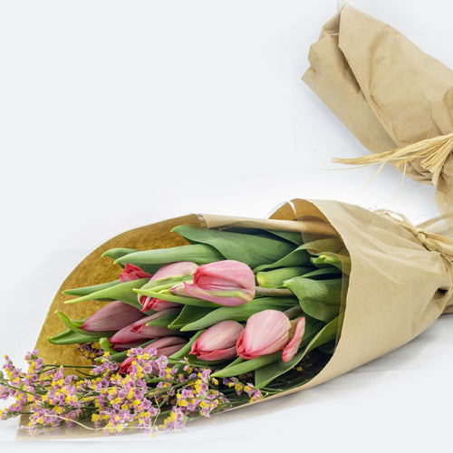 Bouquet of pink tulips and green leaves wrapped in brown paper on a white background