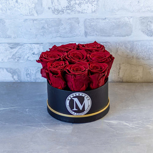 Black box with red roses on a gray surface with a light gray brick wall background