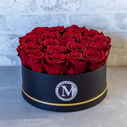 Black round box with red roses on a gray surface with a light gray textured wall background