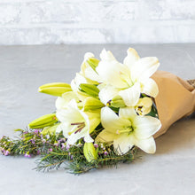 Load image into Gallery viewer, Bouquet of white flowers wrapped in brown paper on a light gray surface
