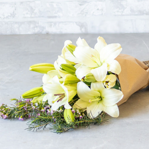 Bouquet of white flowers wrapped in brown paper on a light gray surface