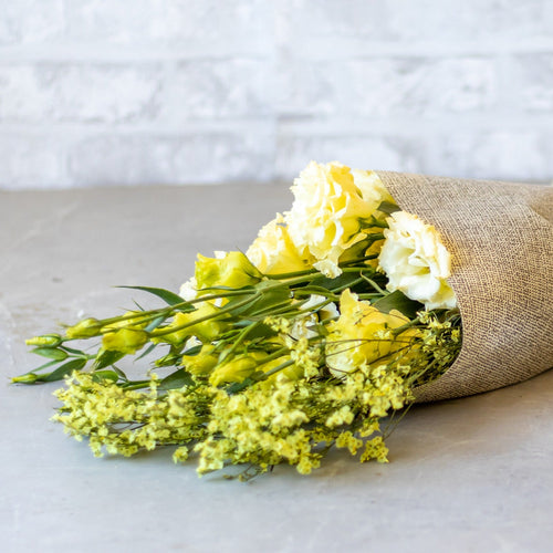 Bouquet of yellow flowers wrapped in burlap on a light surface with a light gray background