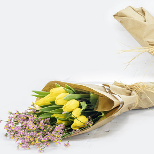 Bouquet of yellow tulips and small purple flowers wrapped in brown paper on a white background